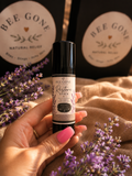 Hand holding a Bee Gone Naturals Restore Stick, a black 0.5 oz tube with a lavender-illustrated label, surrounded by fresh lavender sprigs